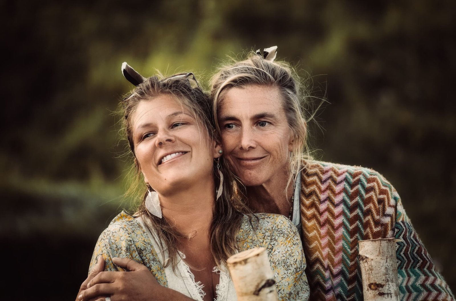 living inquiry by tomm claude Zwei Frauen stehen im Freien, lächeln und umarmen sich. Beide tragen gemusterte Schals und Federohrringe. Ihre Freundschaft und Verbundenheit heben sich deutlich von dem verschwommenen grünen Laub im Hintergrund ab. spirituelles coaching und zen meditation für emotionale heilung, erwachen und essenz