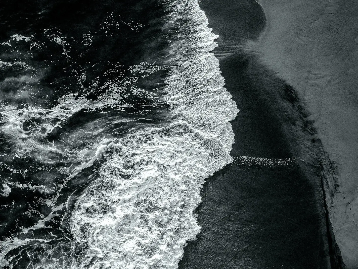 living inquiry by tomm claude Schwarz-Weiß-Luftaufnahme von Meereswellen, die auf einen Sandstrand prallen, Schaum entlang des Ufers und Fußabdrücke im Sand, die ein Gefühl von spirituellem Coaching und Zen-Meditation für emotionale Heilung und Embodiment hervorrufen. spirituelles coaching und zen meditation für emotionale heilung und embodiment