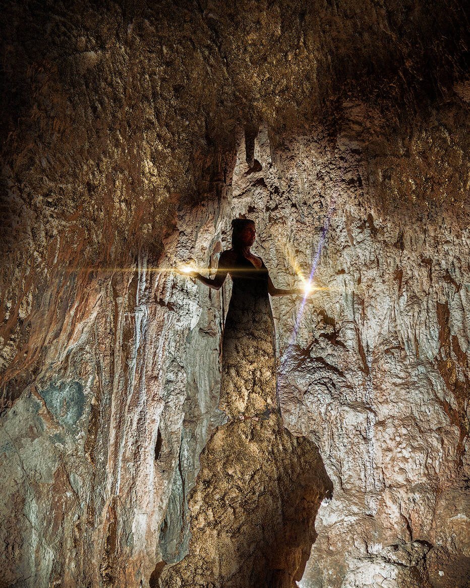 spirituelles coaching und zen meditation für emotionale heilung und embodiment Eine Person steht in einer zerklüfteten Höhle, die von einem Lichtstrahl beleuchtet wird, der eine dramatische Silhouette vor den strukturierten Felswänden erzeugt - eine Atmosphäre, die an Zazen-Meditation inmitten von zerklüfteten Kanten und erdigen Tönen erinnert.