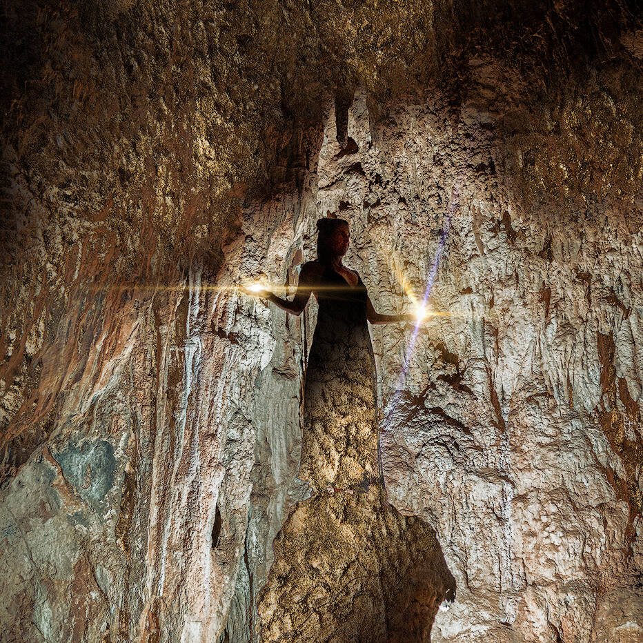 spirituelles coaching und zen meditation für emotionale heilung und embodiment Eine Person steht in einer zerklüfteten Höhle, die von einem Lichtstrahl beleuchtet wird, der eine dramatische Silhouette vor den strukturierten Felswänden erzeugt - eine Atmosphäre, die an Zazen-Meditation inmitten von zerklüfteten Kanten und erdigen Tönen erinnert.