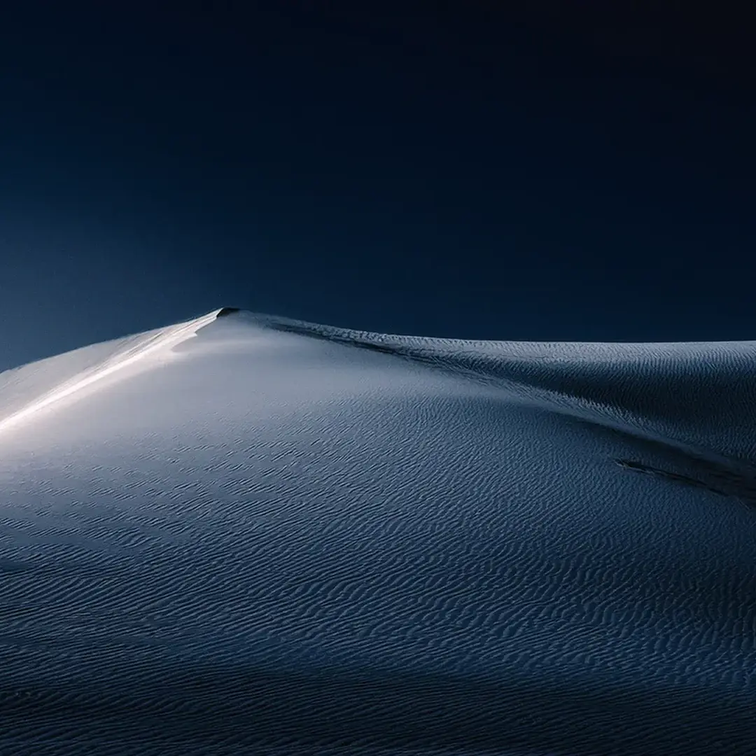 spirituelles coaching und zen meditation für emotionale heilung und embodiment Wogende Sanddünen unter einem dunklen, tiefblauen Himmel bei Nacht. Das weiche Mondlicht wirft sanfte Schatten und fördert ein Gefühl von Heilung und Ruhe, das die Gelassenheit des spirituellen Coachings widerspiegelt.