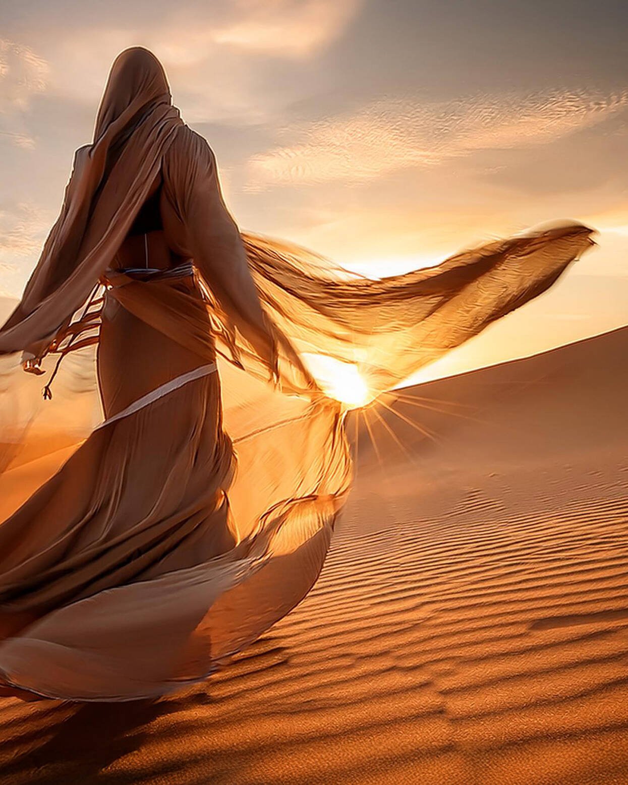 spirituelles coaching und zen meditation für emotionale heilung und embodiment Eine in fließenden, durchscheinenden Stoff gehüllte Person läuft bei Sonnenuntergang über Sanddünen, wobei das Sonnenlicht die Figur beleuchtet und lange Schatten auf die gewellte Wüstenlandschaft wirft.