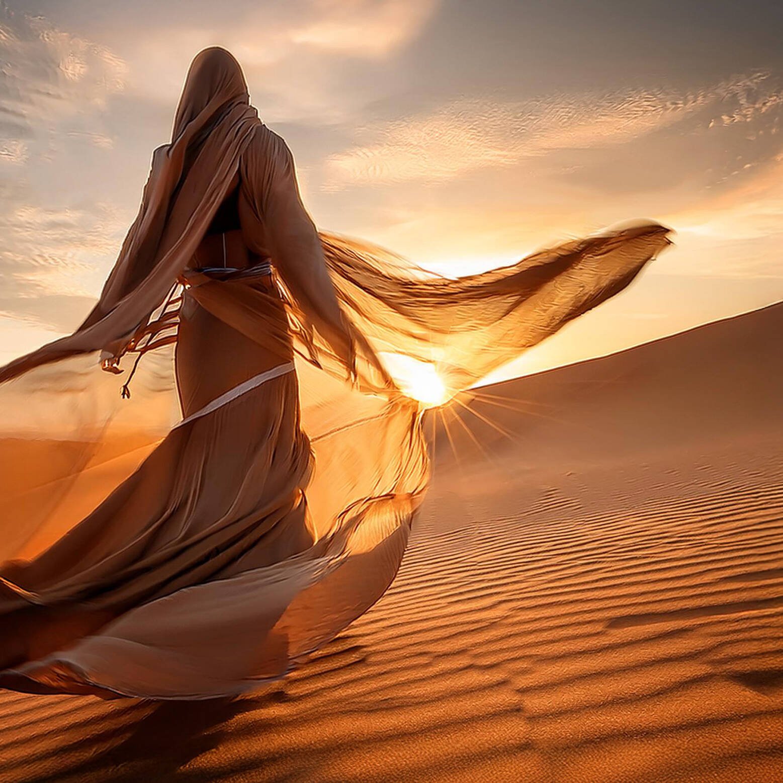 spirituelles coaching und zen meditation für emotionale heilung und embodiment Eine in fließenden, durchscheinenden Stoff gehüllte Person läuft bei Sonnenuntergang über Sanddünen, wobei das Sonnenlicht die Figur beleuchtet und lange Schatten auf die gewellte Wüstenlandschaft wirft.
