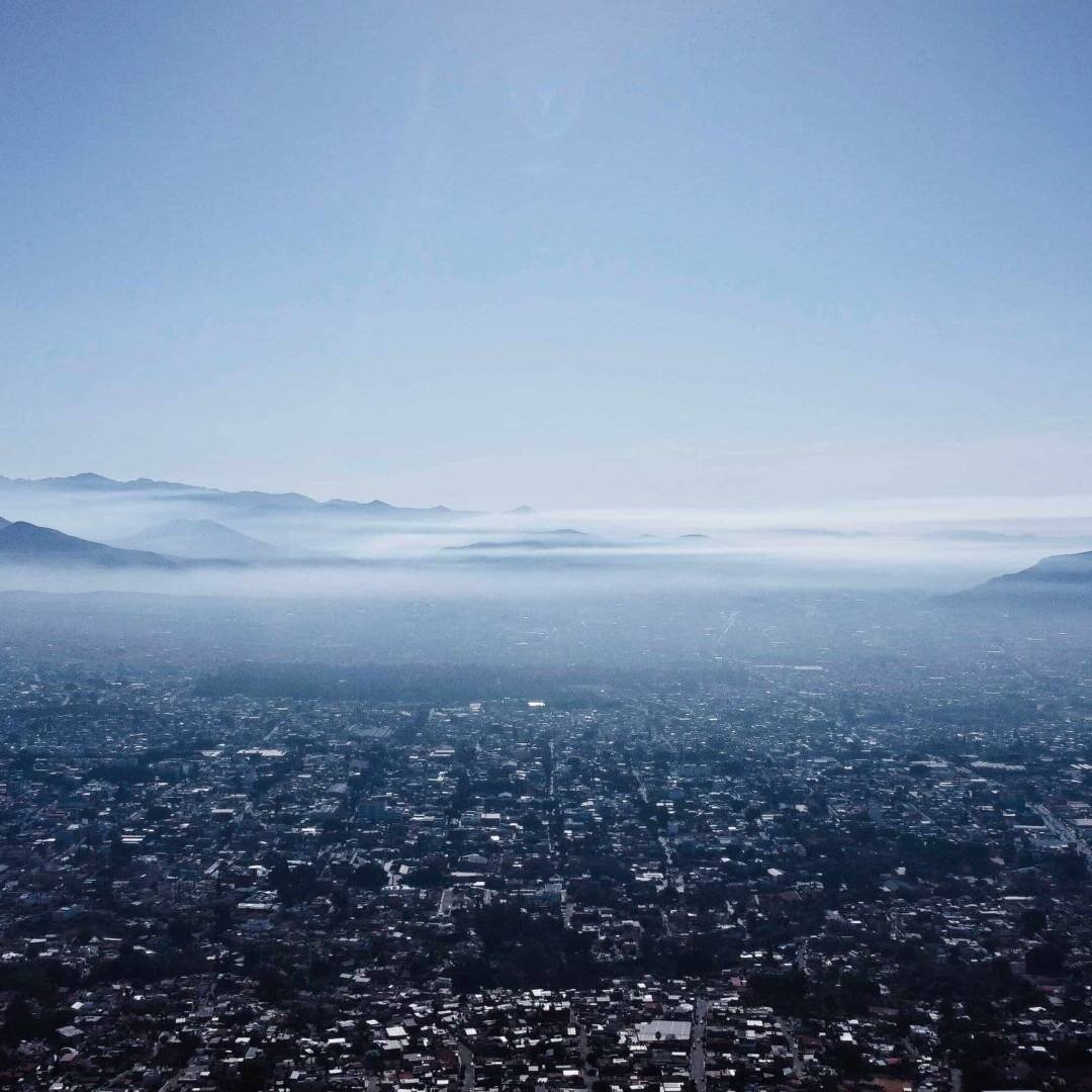 living inquiry by tomm claude Luftaufnahme einer Stadt mit einer dichten urbanen Landschaft, umgeben von Bergen unter einem dunstigen Himmel. Nebel liegt zwischen den Hügeln und spiegelt das ruhige Gleichgewicht zwischen Grenzen setzen und Selbstentdeckung in dieser ruhigen, weitläufigen Szene wider. spirituelles coaching und zen meditation für emotionale heilung, erwachen und essenz