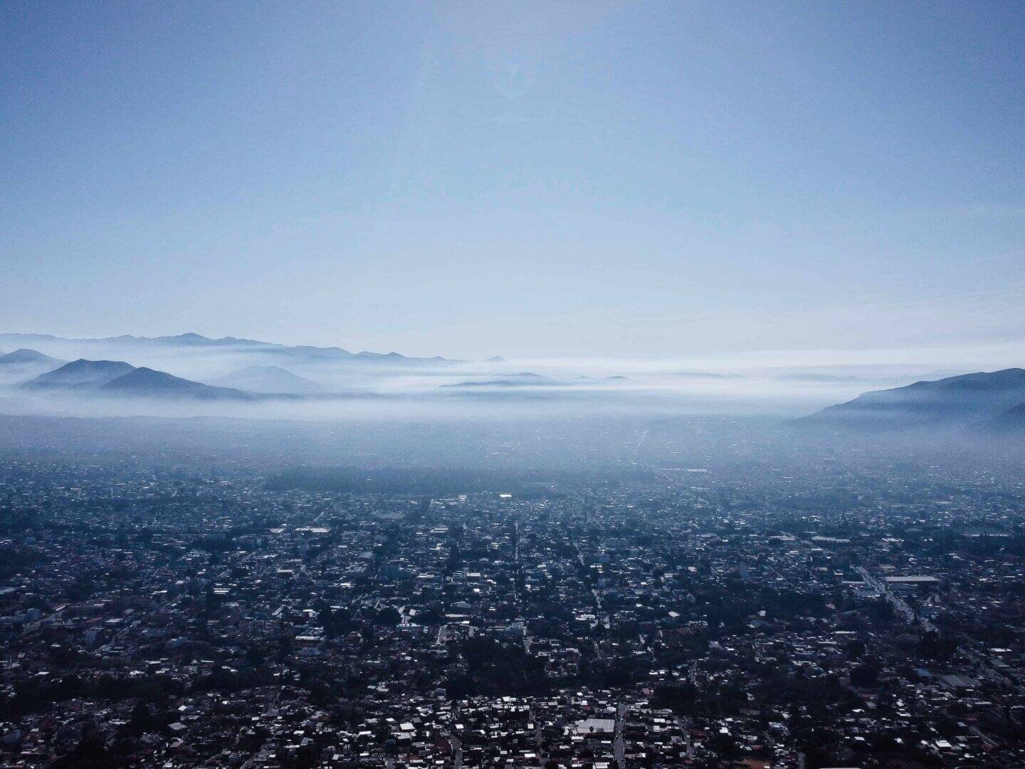 living inquiry by tomm claude Luftaufnahme einer Stadt mit einer dichten urbanen Landschaft, umgeben von Bergen unter einem dunstigen Himmel. Nebel liegt zwischen den Hügeln und spiegelt das ruhige Gleichgewicht zwischen Grenzen setzen und Selbstentdeckung in dieser ruhigen, weitläufigen Szene wider. spirituelles coaching und zen meditation für emotionale heilung, erwachen und essenz